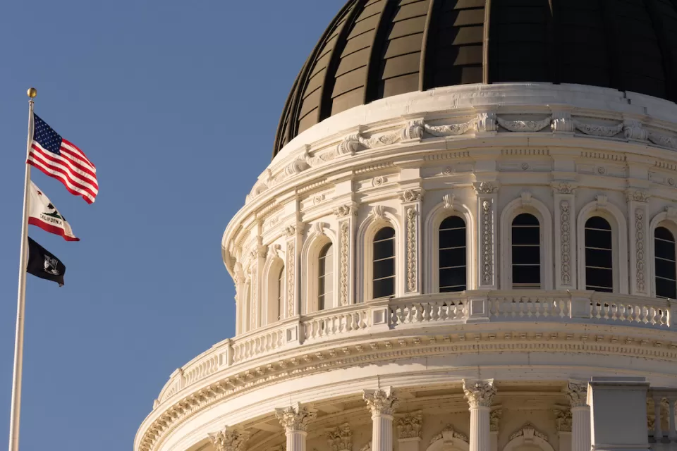 Close-up of Californis state capitol dome with U.S., California, and POW/MIA flags on flagpole.